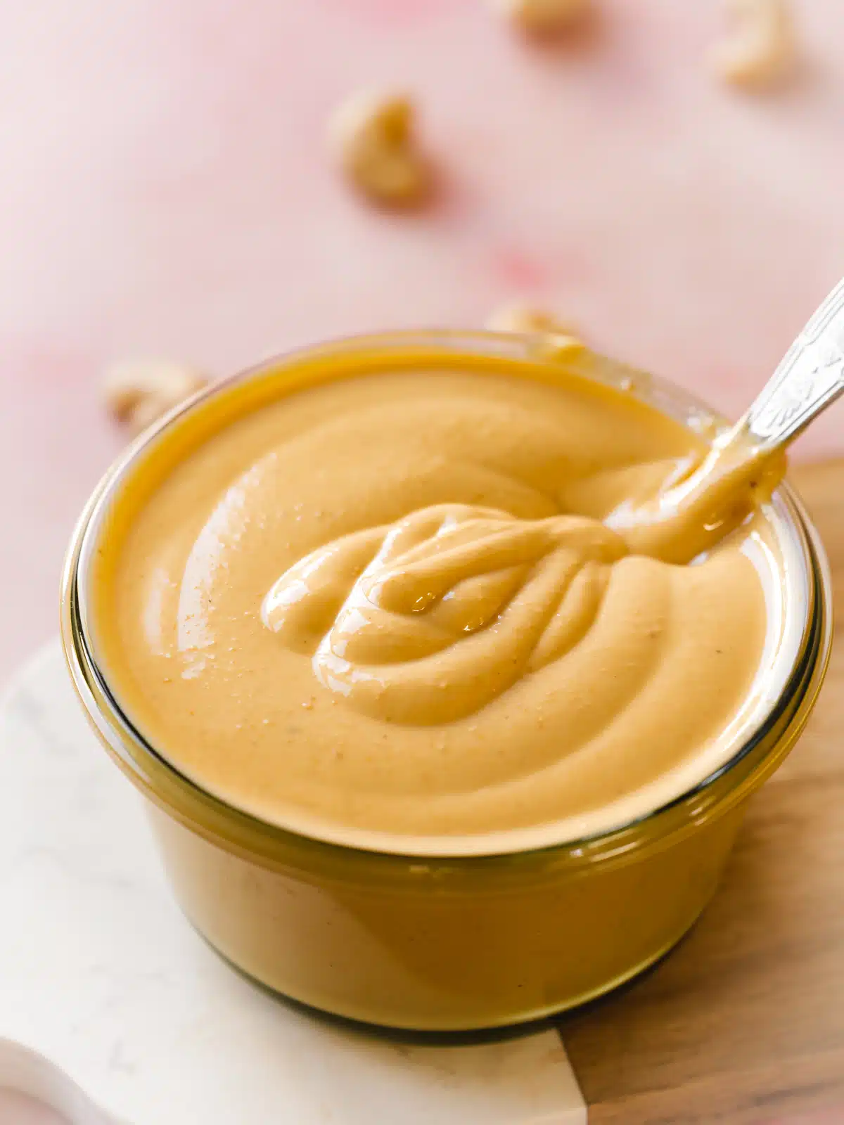 thick and creamy homemade cashew butter in a clear jar with raw cashews scattered around it.