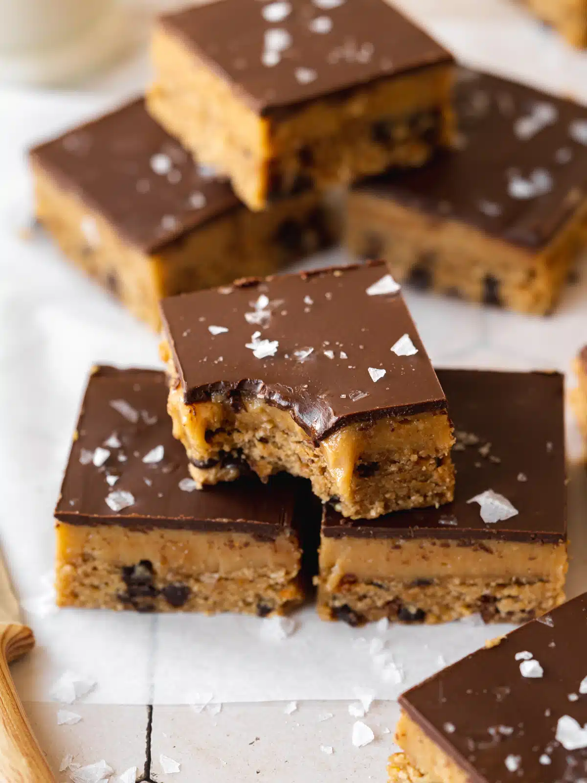 a stack of three vegan cookie dough bars topped with chocolate and flaky sea salt.