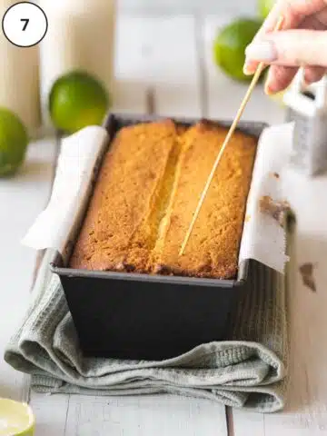 Baked key lime loaf cake being poked with a wooden skewer while still warm from the oven.