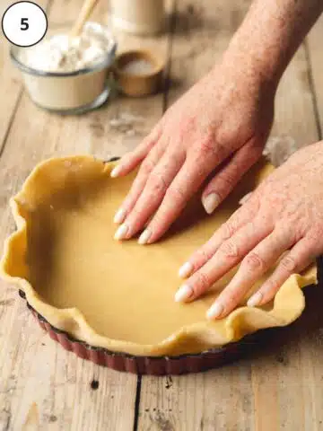 hands carefully pressing rolled out pastry dough into a tart tin.