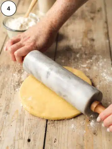 rolling out shortcrust pastry with a grey marble rolling pin on a wooden surface.