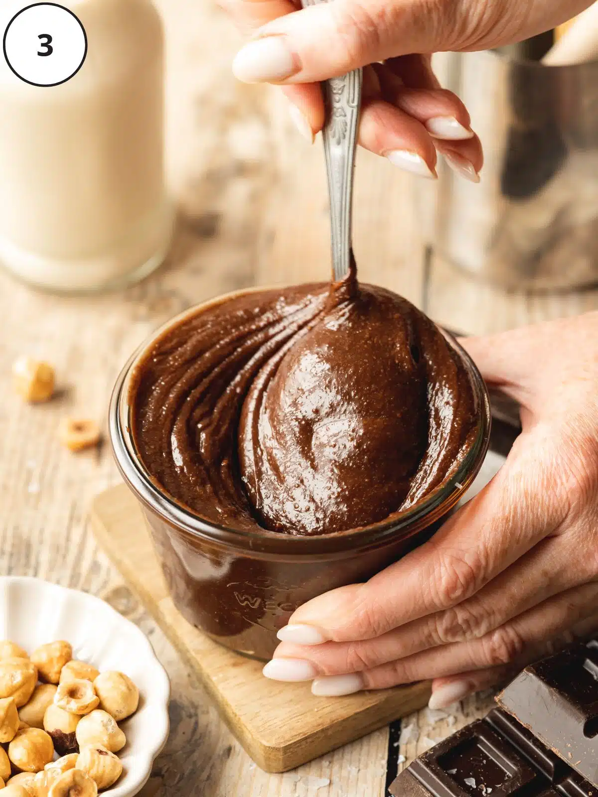 Woman’s hands doling out a spoon of vegan nutella from the glass jar.