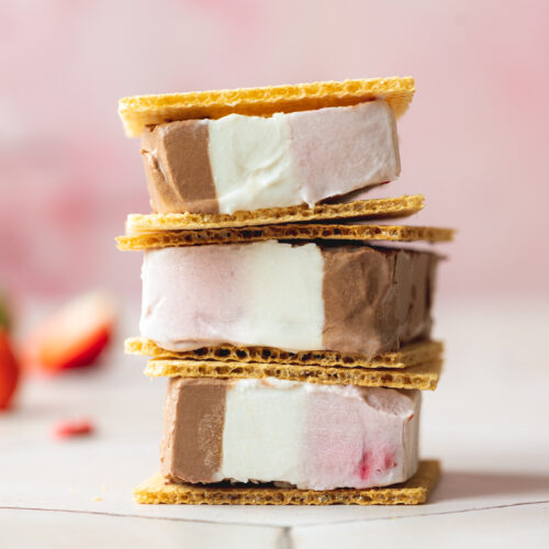 a stack of three vegan neapolitan ice cream sandwiches in wafers with strawberry, vanilla, and chocolate ice cream.