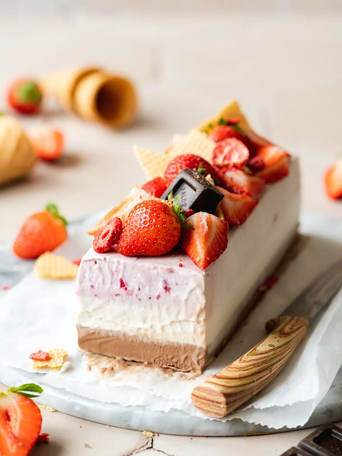 chocolate vanilla strawberry ice cream cake topped with dark chocolate and fresh strawberries on a cutting board.