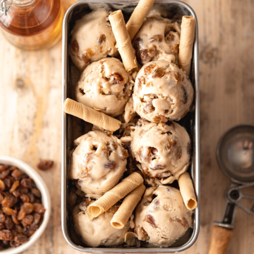 Overhead hero shot of lots of scoops of homemade rum raisin ice cream in a loaf tin adorned with pirouline cookies.