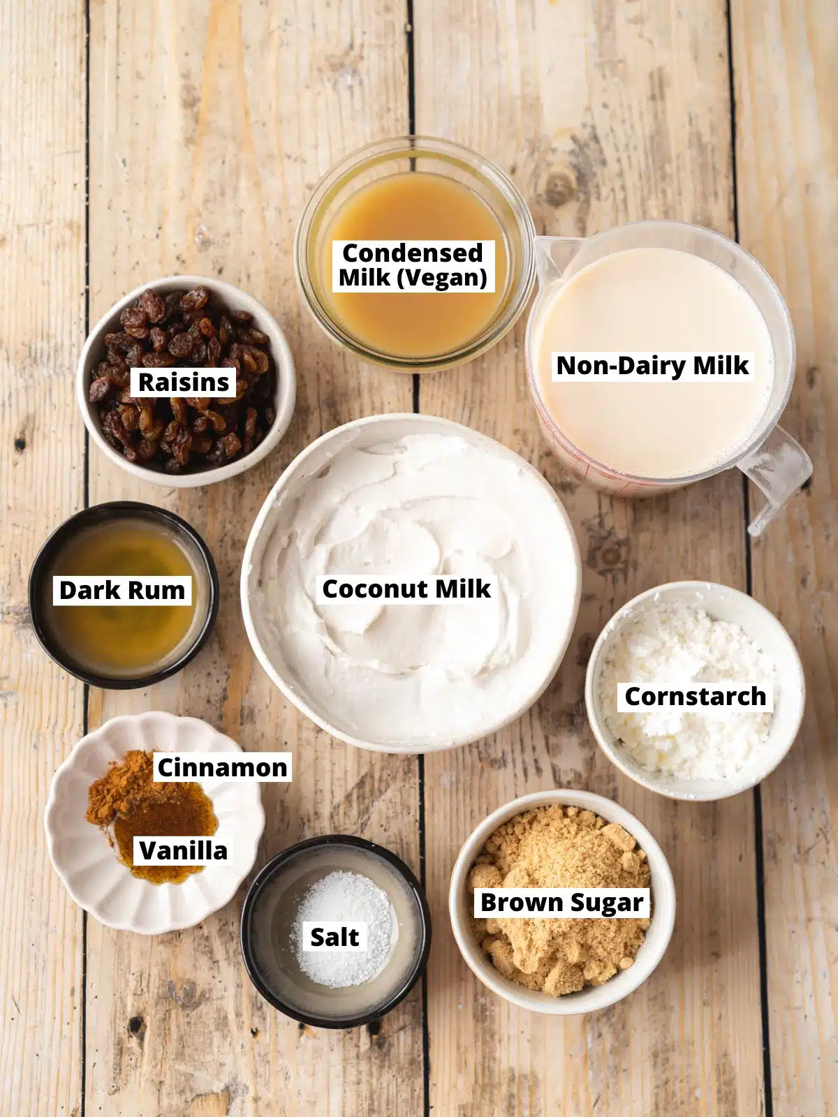 Ingredients needed to make vegan rum and raisin ice cream measured out into bowls on a wooden table with text overlay.