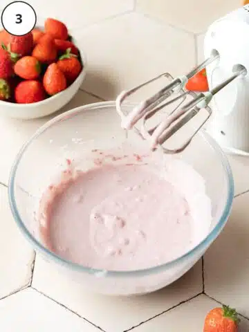 vegan no churn strawberry ice cream in a large mixing bowl with an electric whisk.