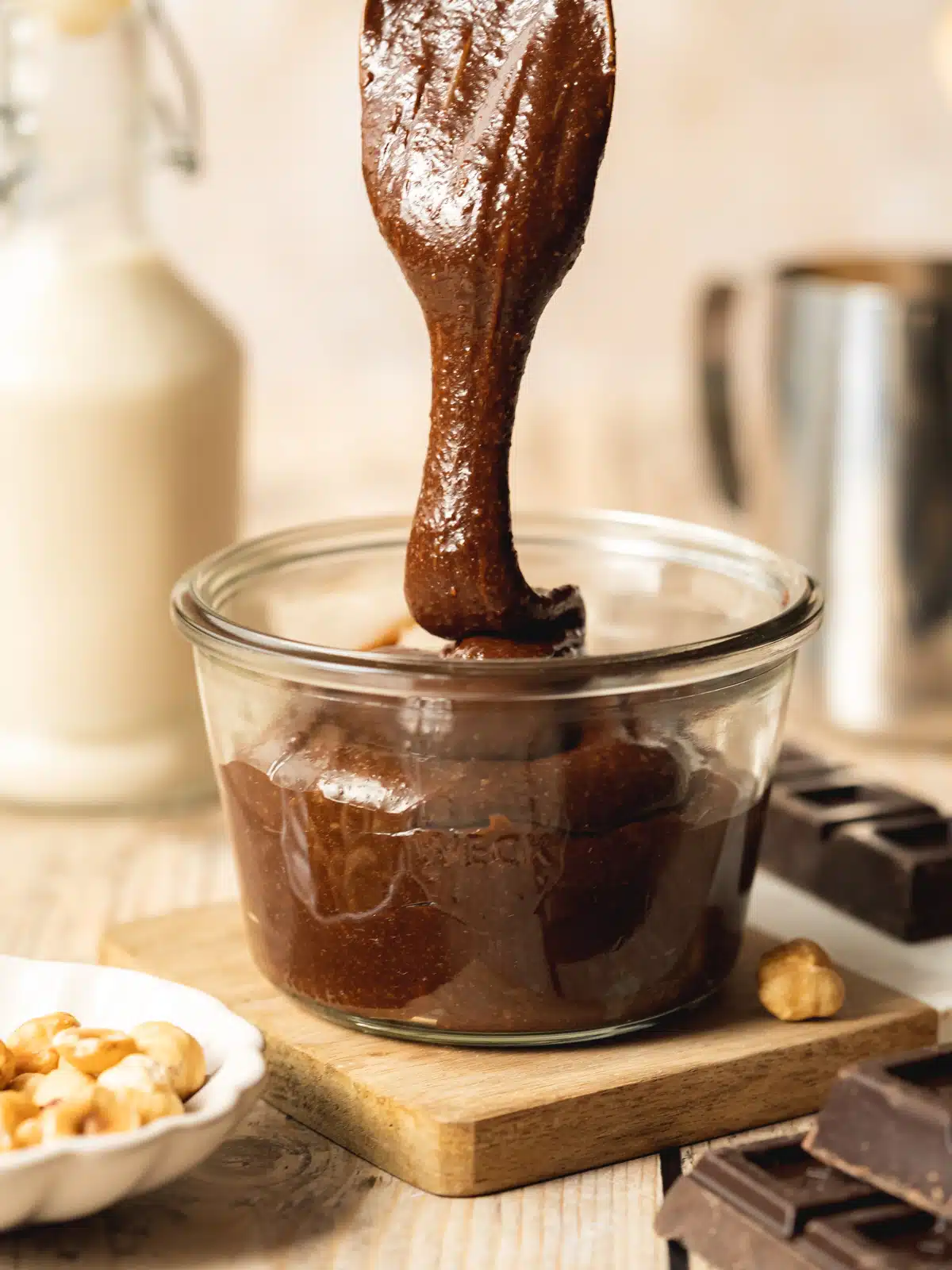 Action shot of warm homemade chocolate hazelnut spread (i.e. Nutella) being drizzled into a glass jar.