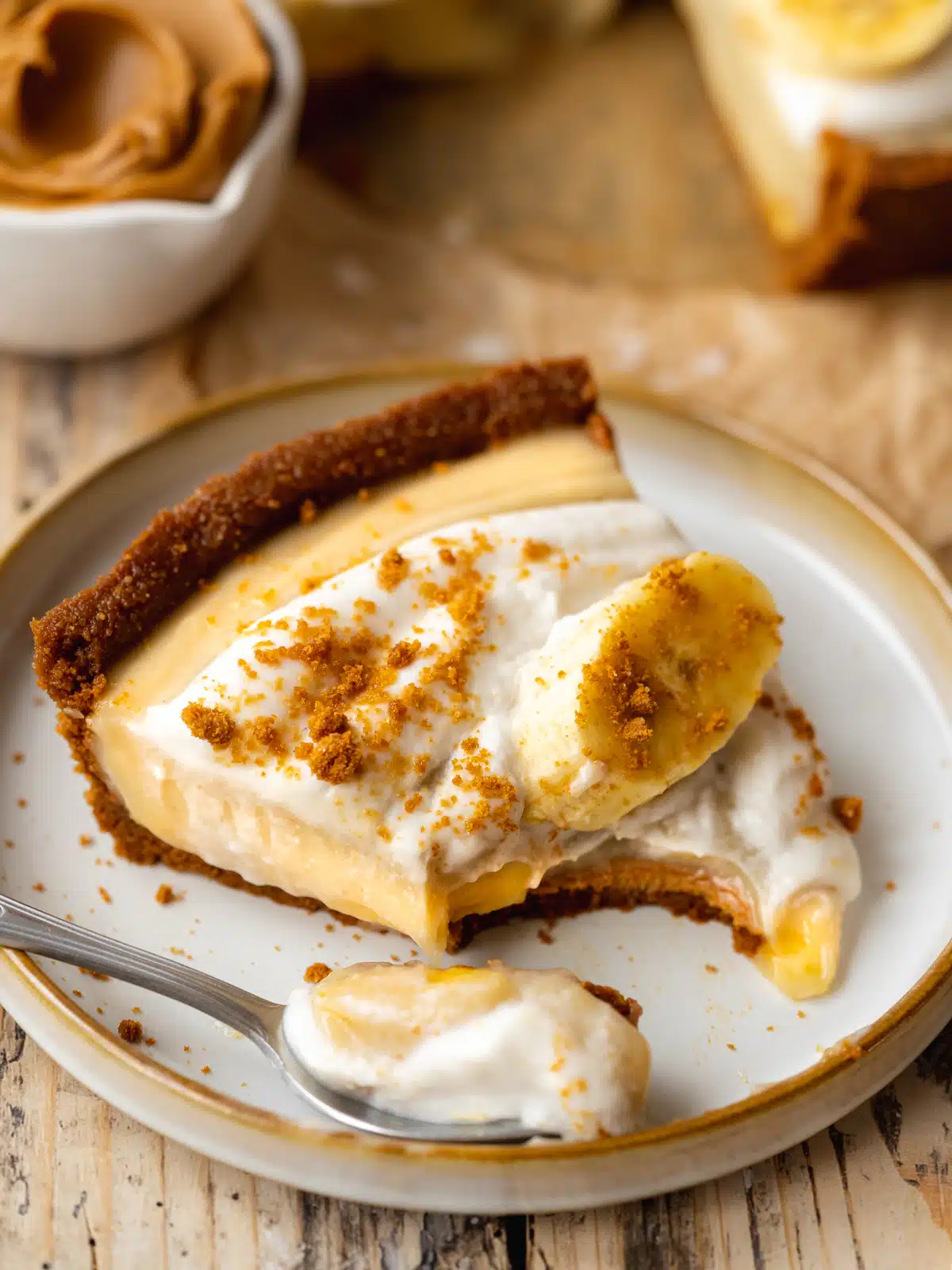 45 degree angle shot of a slice of vegan banana cream pie on a hand-hewn dessert plate with a spoonful taken out to show the distinct layers.