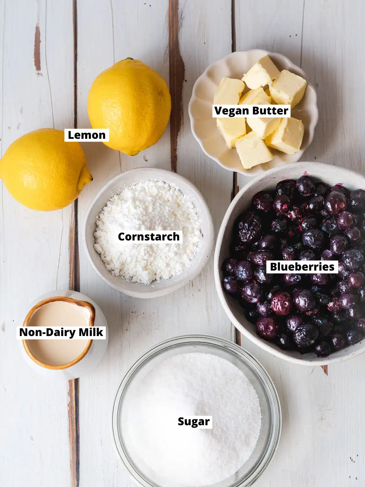 ingredients for homemade blueberry curd measured out in bowls on a white wooden surface.