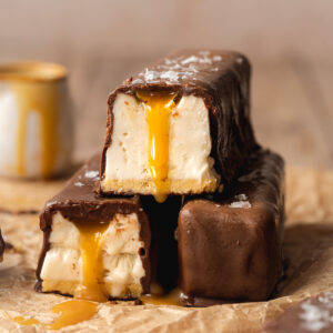 three homemade twix ice cream bars stacked on top of one another with caramel dripping from inside them.