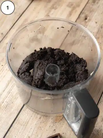 Oreo cookie crust mixture in the base of a food processor after adding butter.