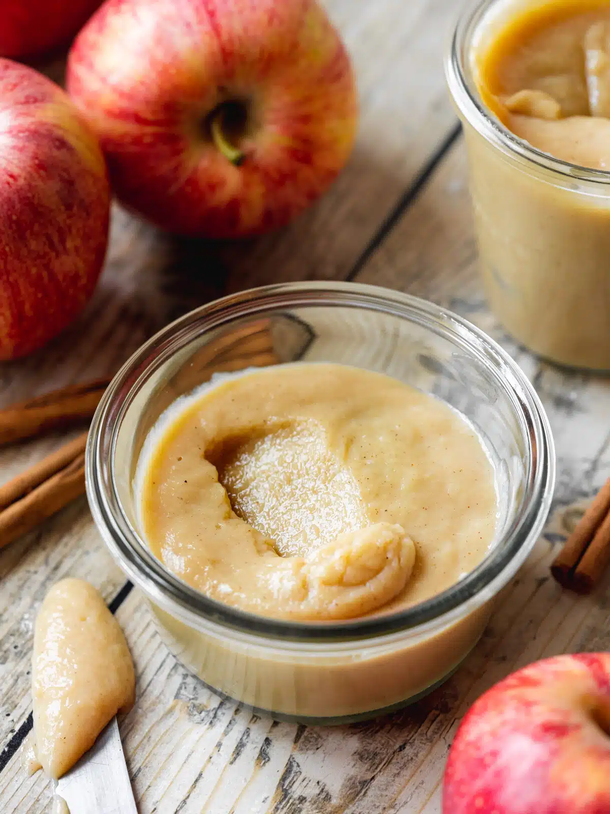 apple curd in a jar thats been set in the fridge with fresh red apples in the background.