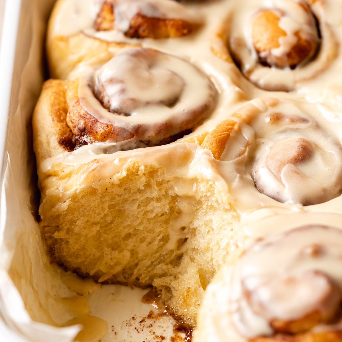 a ceramic dish with soft vegan cinnamon rolls with icing, and one lifted away showing the soft texture.