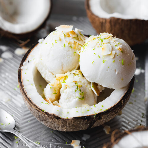 three scoops of fresh coconut sorbet in a coconut half topped with lime zest and toasted coconut flakes.