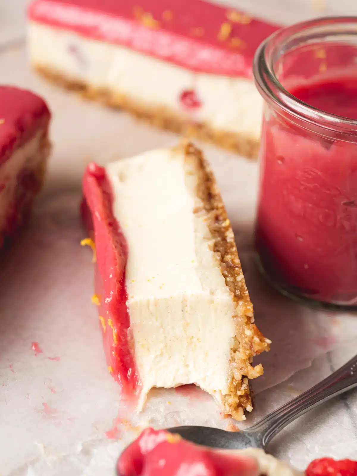 a slice of no bake lemon cheesecake with raspberry curd topping on its side with a spoonful taken showing the creamy consistency.