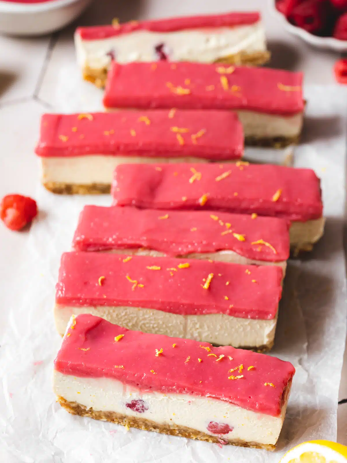 raspberry cheesecake slices topped with bright raspberry curd on crunched up parchment paper.