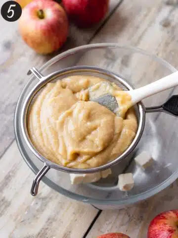 vegan apple curd in a fine-mesh sieve on top of a mixing bowl with cubes of cold butter.