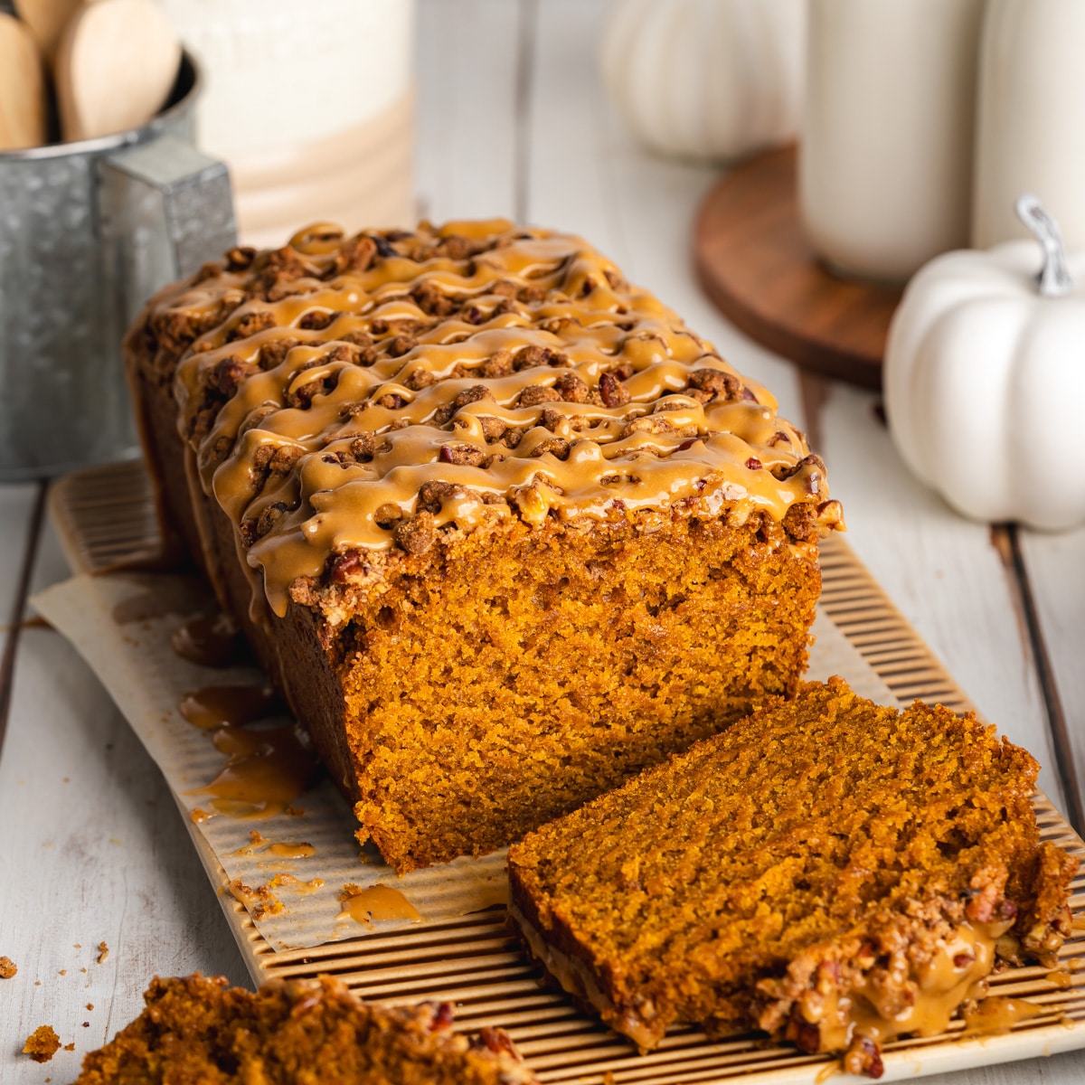 a loaf of vegan pumpkin bread with a slice taken from it showing the fluffy texture, It has a biscoff glaze and pecan streusel topping.