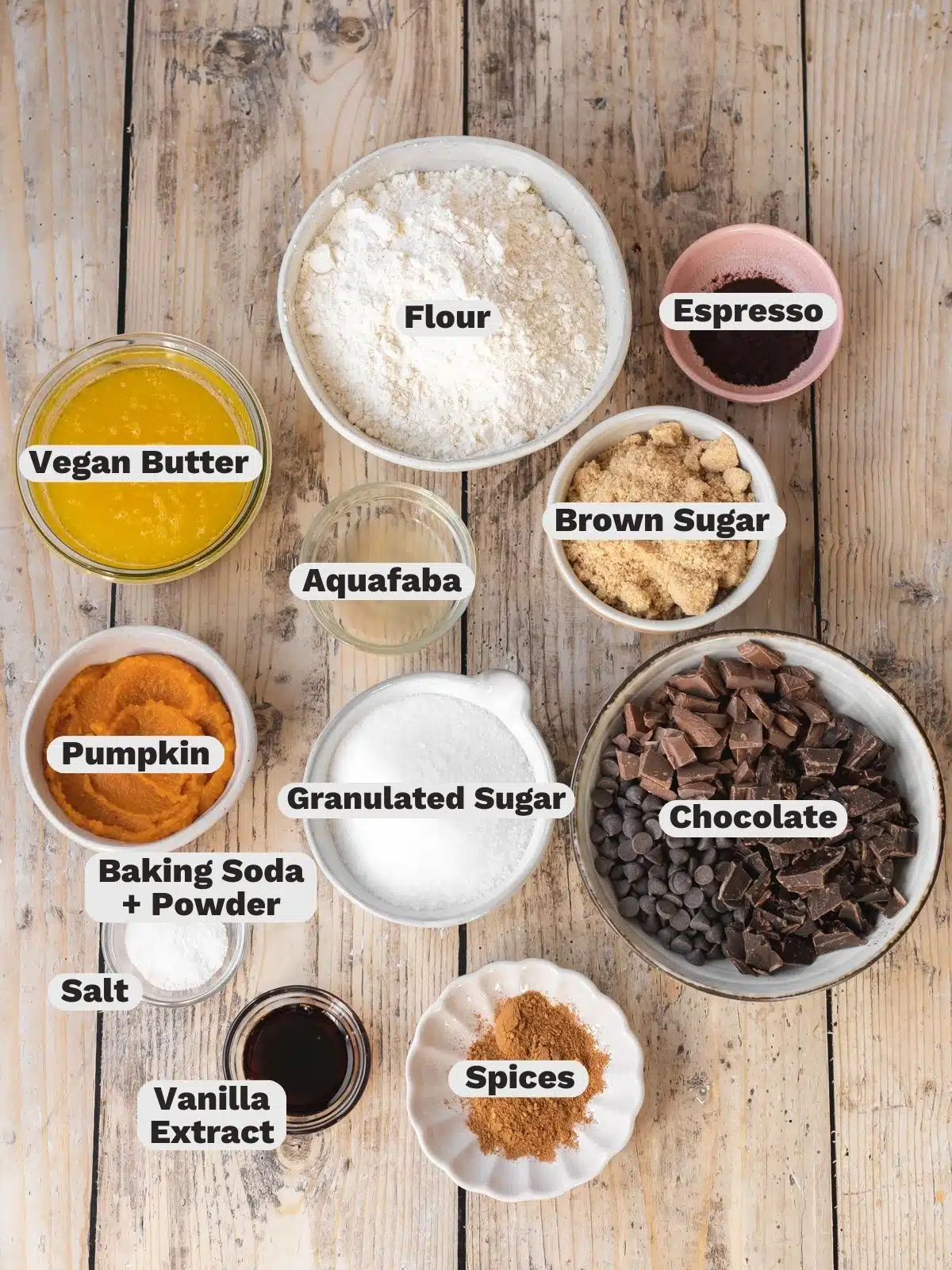Flat lay shot of ingredients needed to make vegan pumpkin chocolate chip cookies measured out into bowls on a wooden table with text overlay.