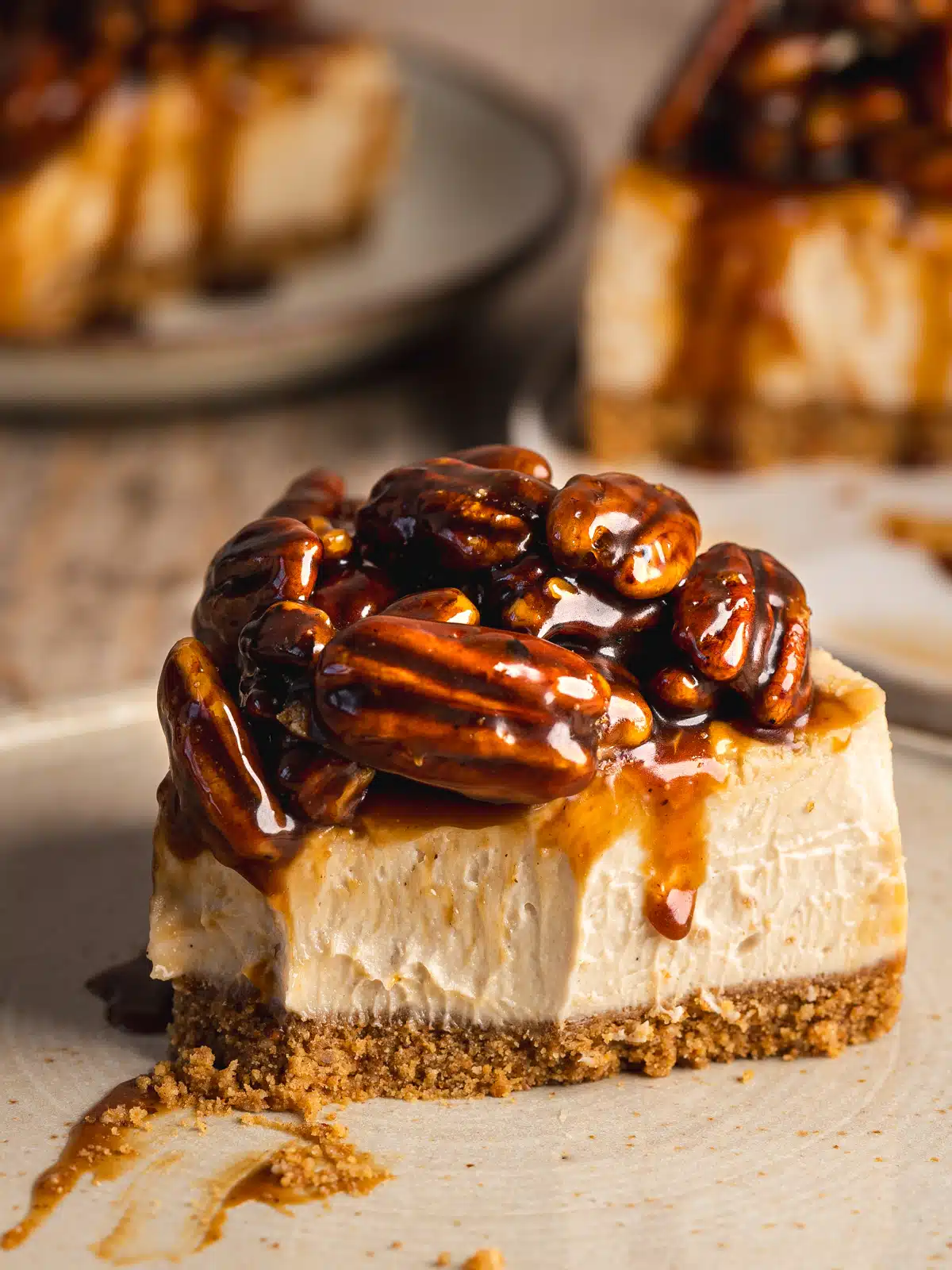 vegan pecan cheesecake on a ceramic plate with caramel pecan topping oozing down the sides. There is a bite taken from the cake, showing the creamy consistency.