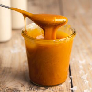 a weck jar with caramel sauce and a spoon pulling some of the caramel away showing the thick consistency.