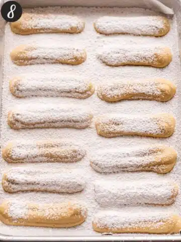 ladyfingers on a baking sheet dusted with icing sugar ready to go into the oven.