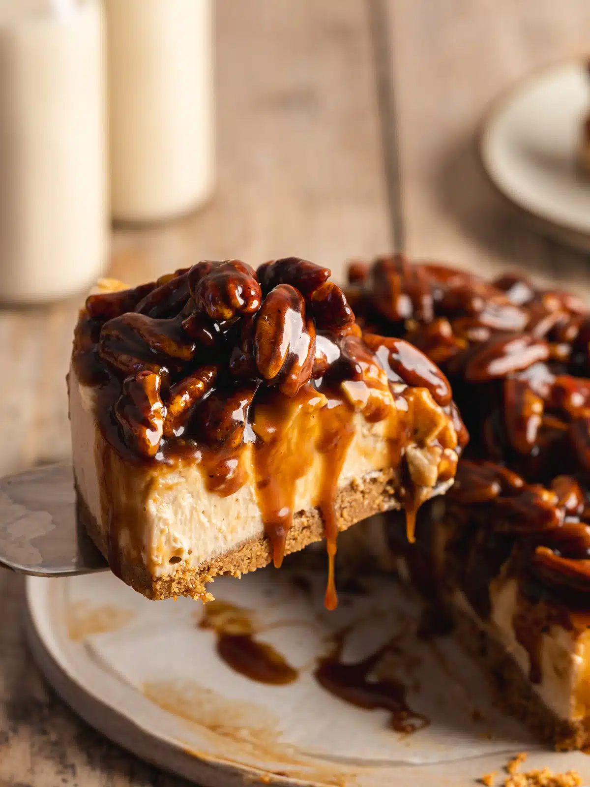 a slice of pecan cheesecake being lifted on a cake slice with caramel sauce dripping down the sides.