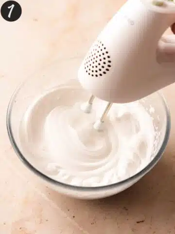 whisking aquafaba in a large mixing bowl with an electric mixer.