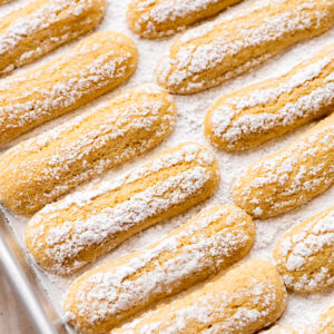freshly baked vegan ladyfinger cookies on a baking tray with a dusting of powdered sugar.