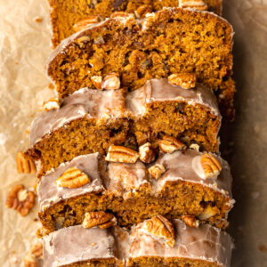 sweet potato bread with icing and pecans on top that's been sliced on scrunched up brown paper.