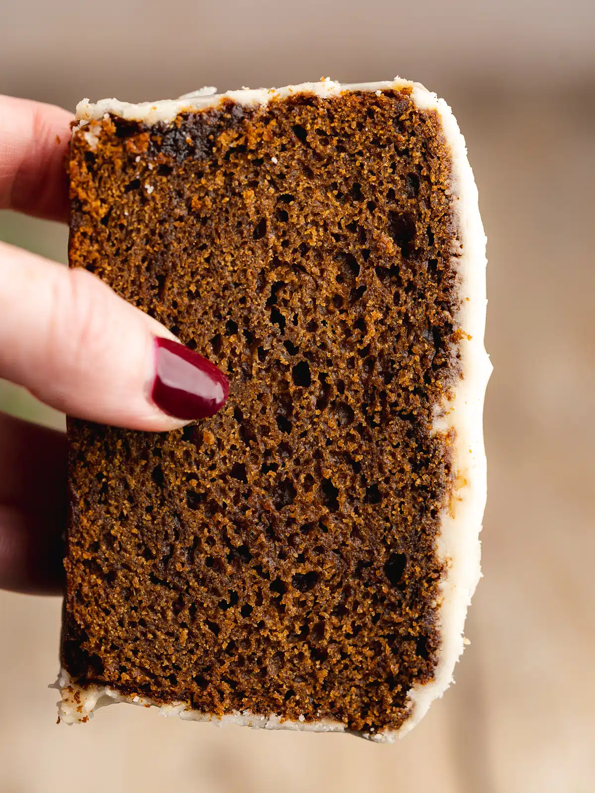 a hand holding up a slice of gingerbread cake with cream cheese icing, showing the moist and fluffy consistency.