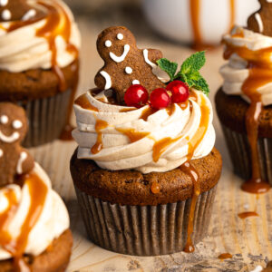 gingerbread cupcakes with swirled frosting and a gingerbread man on top. There is caramel drizzled and a mint leaf on top of them.