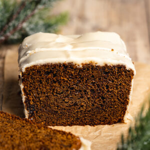 a loaf of gingerbread cake with cream cheese frosting and a few slices taken from it.