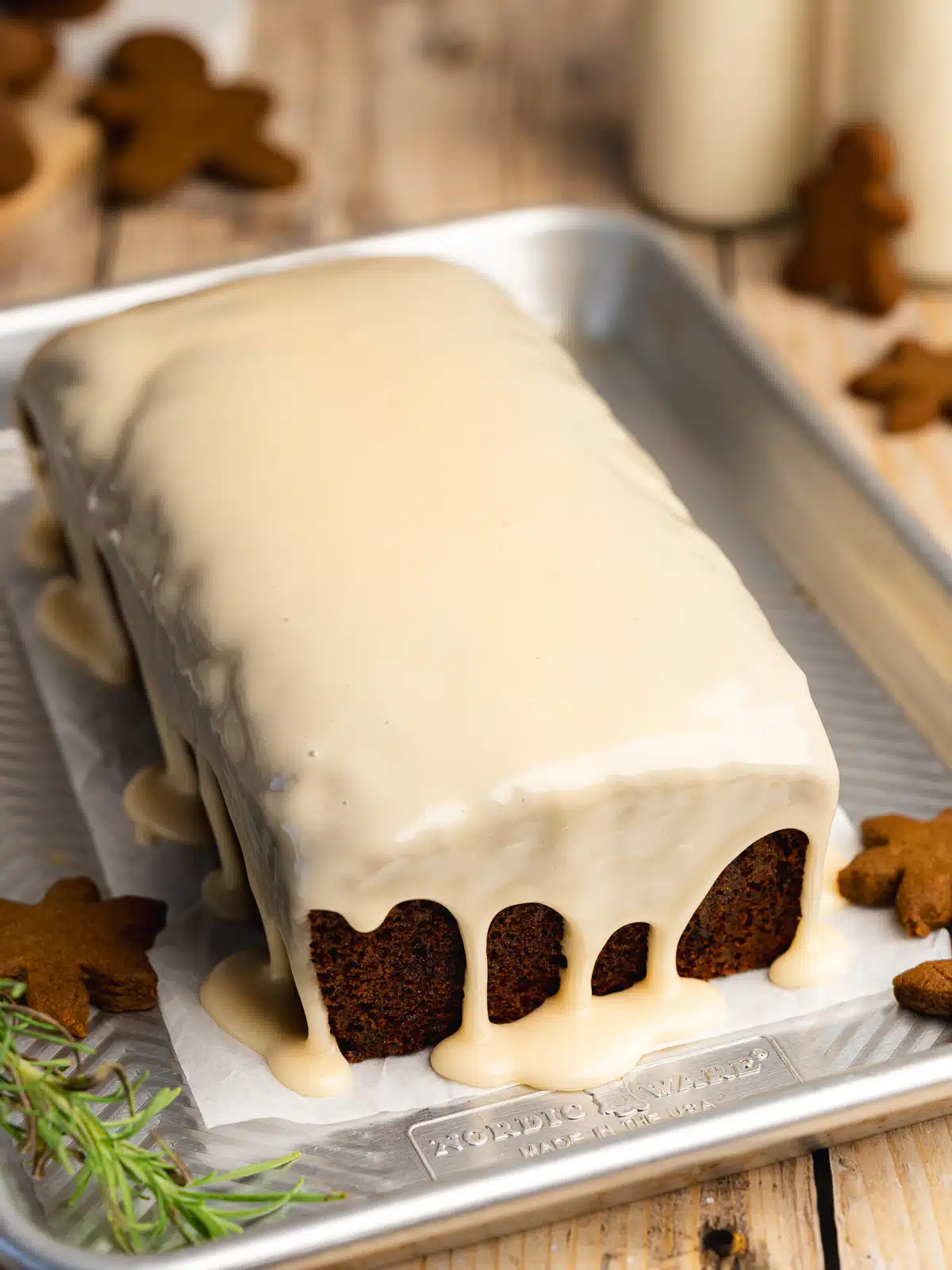 gingerbread loaf cake on a metal tray with cream cheese icing poured on top, and dripping down the sides.