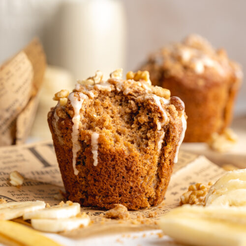 a banana muffin with walnut streusel topping and vanilla icing on scrunched up parchment paper with small bottles of milk in the background.