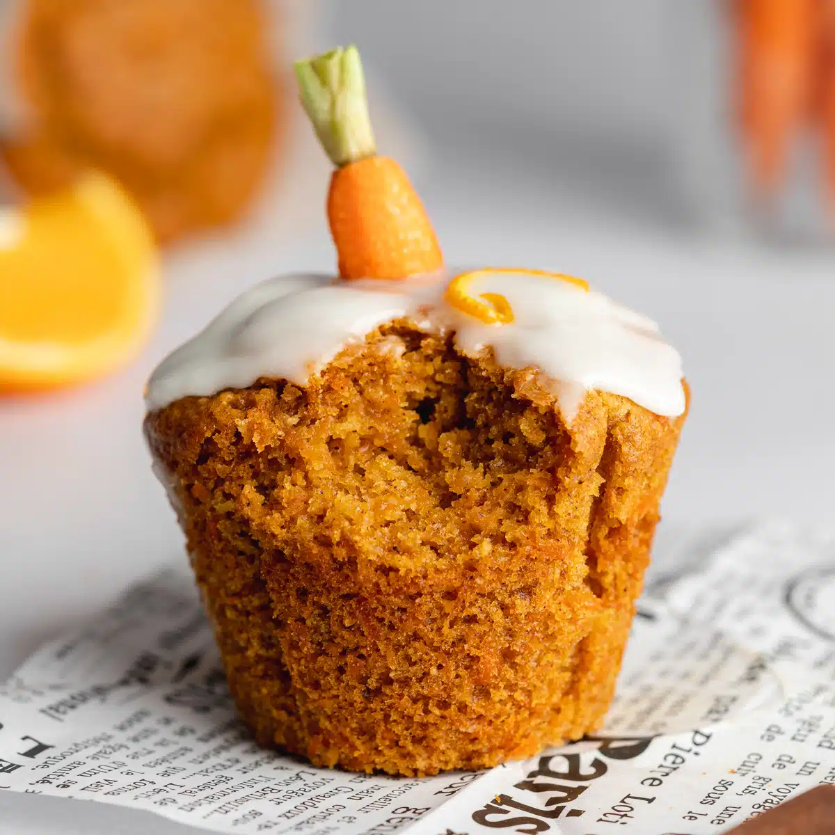 a carrot muffins with icing and a mini carrot on top with a bite taken from it.