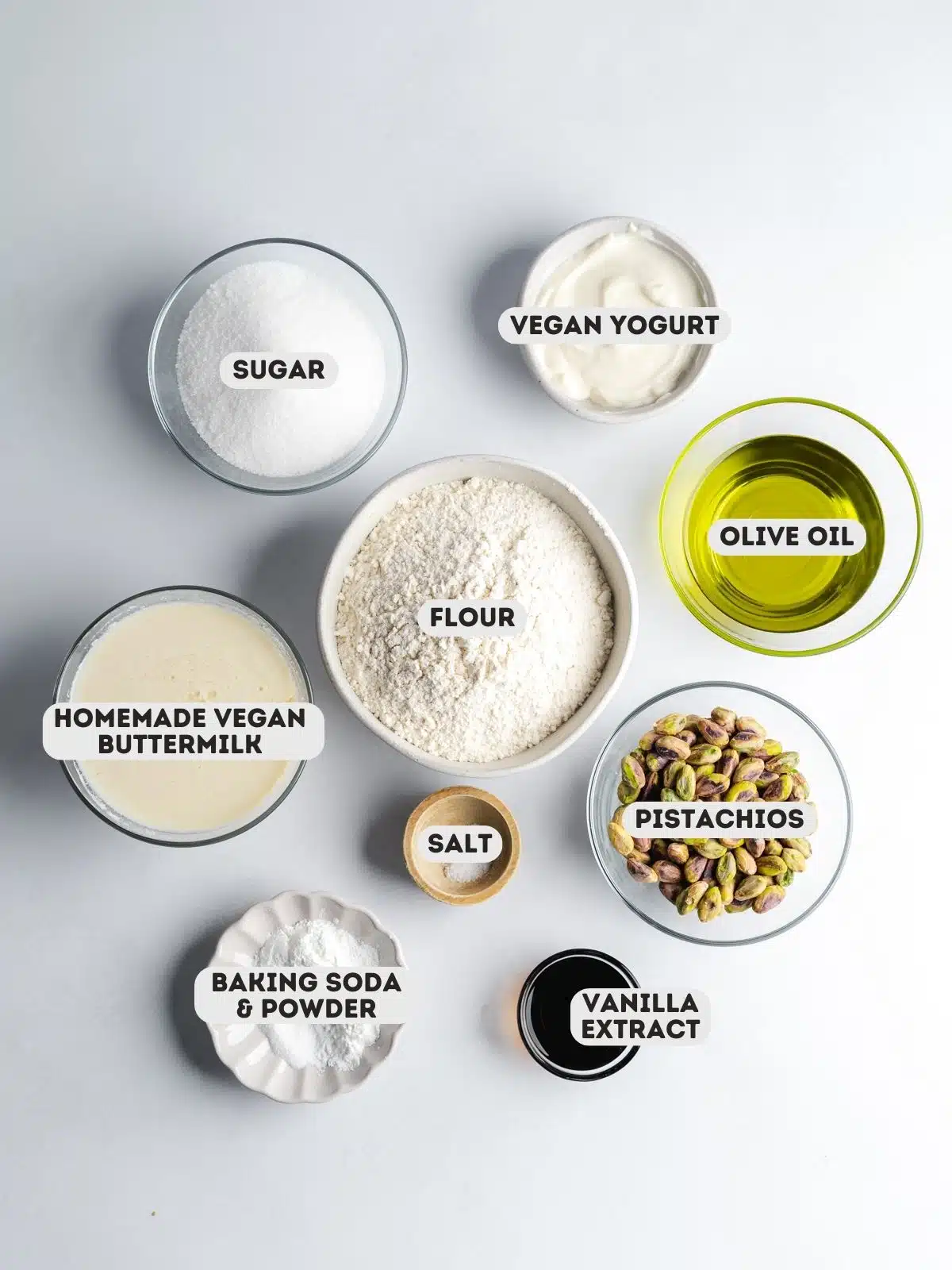ingredients to make pistachio muffins measured in clear bowls on a gray surface with text overlay.