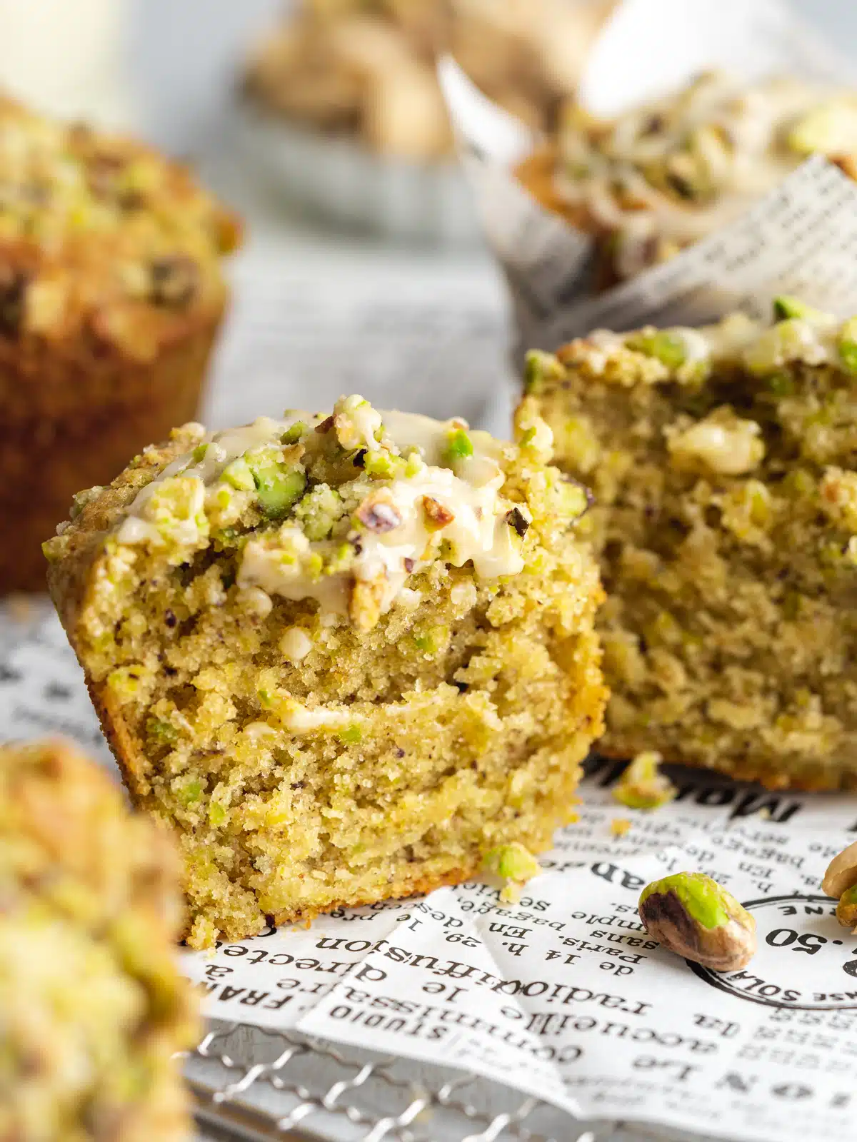a pistachio muffin sliced in half showing the soft and fluffy crumb interior with pistachios scattered around the scene.