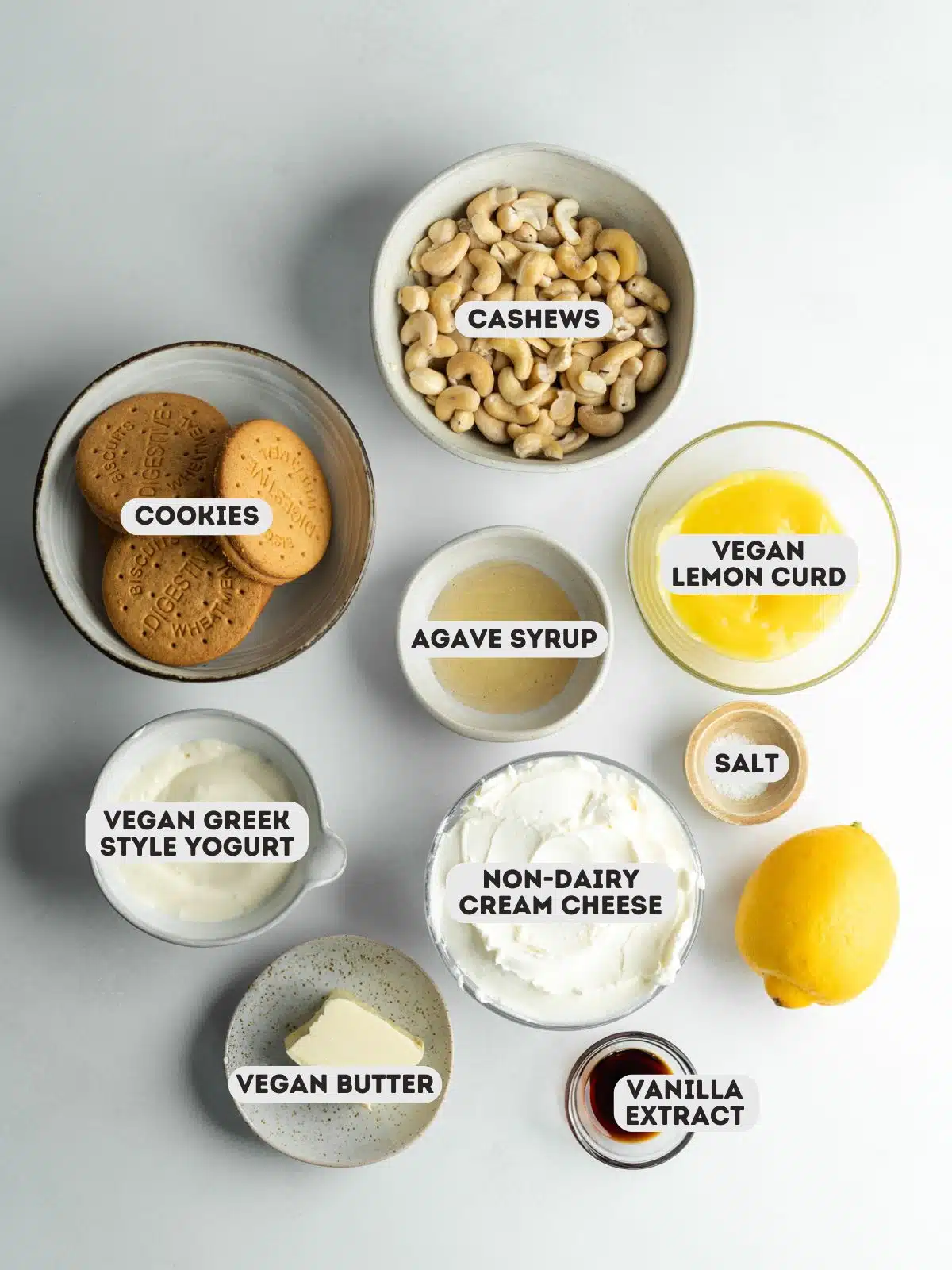 ingredients for vegan lemon cheesecake measured out in bowls on a gray surface.