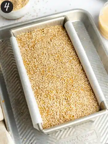 a loaf of tahini bread topped with sesame seeds on an aluminium tray before baking.