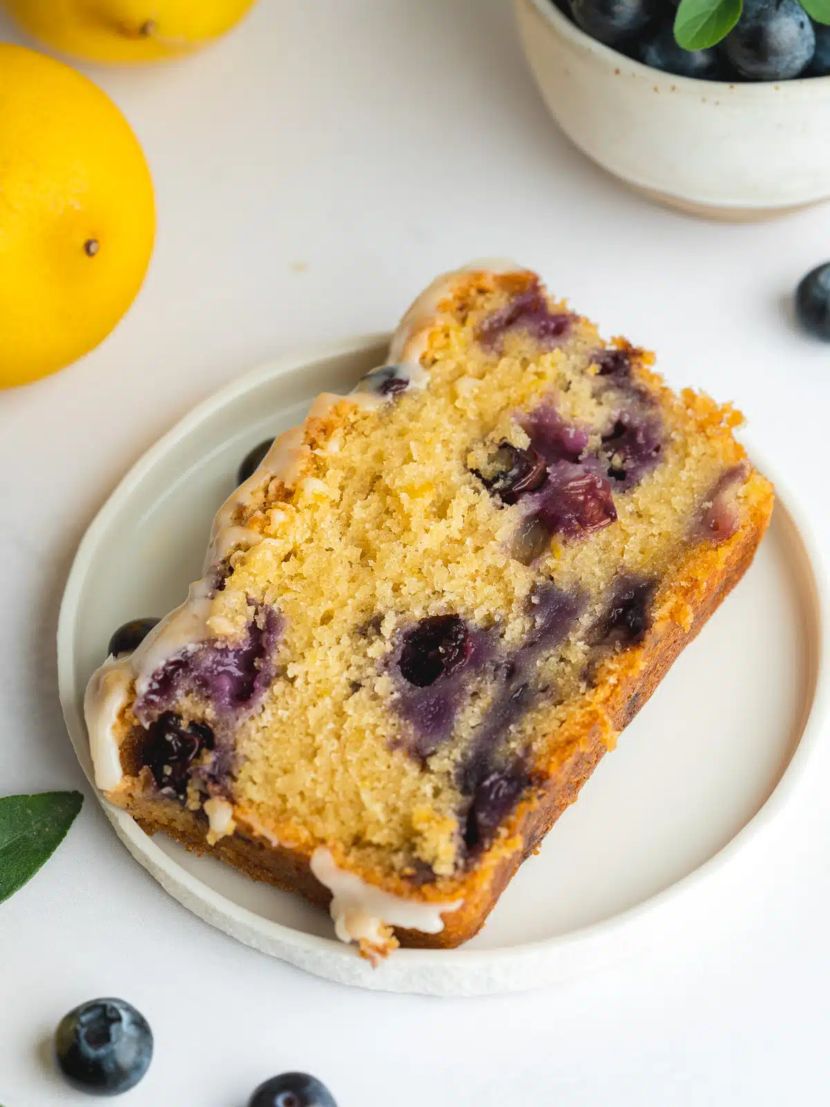 a slice of vegan blueberry bread with frosting on a plate.
