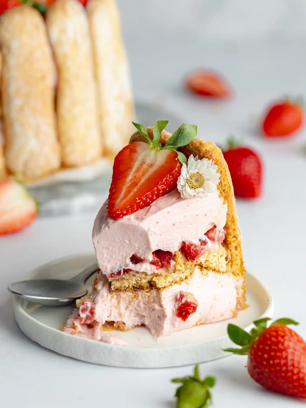 a slice of strawberry charlotte cake on a small dessert plate with a spoonful taken from it showing the creamy texture.
