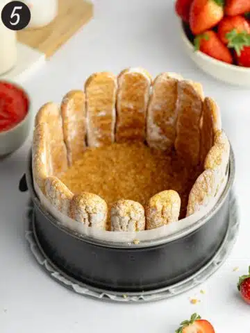 a lined cake pan with ladyfingers lined around the edges before being filled with strawberry mousse.