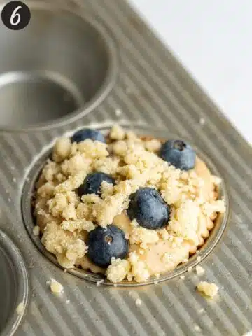 blueberry muffins with crumble topping in a muffin tin before baking.
