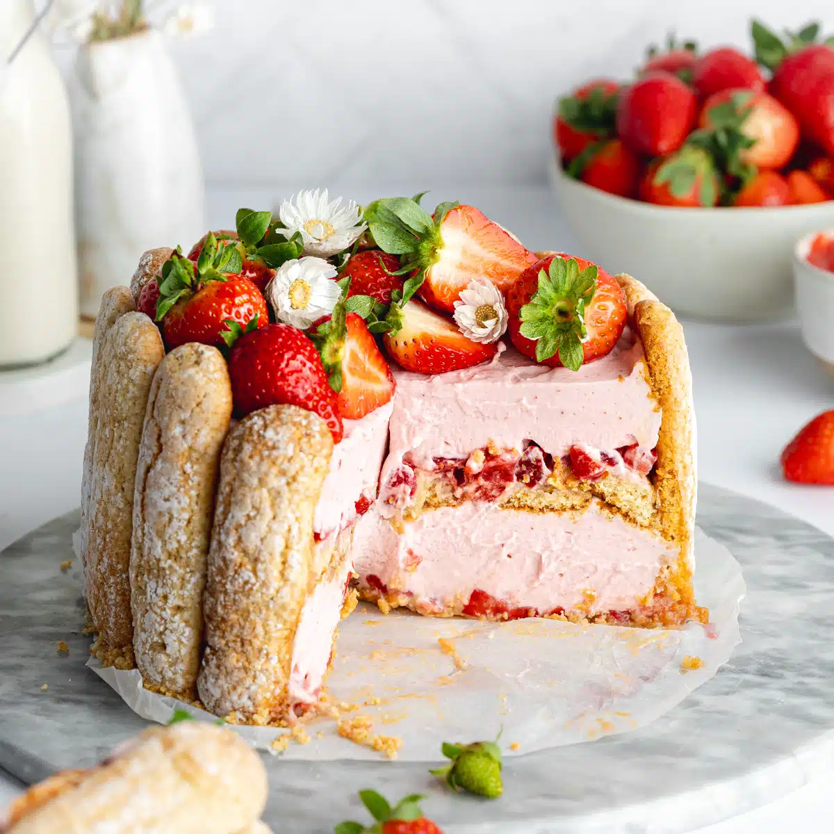 a strawberry charlotte cake topped with fresh berries and with a few slices taken from it showing the layered creamy interior.