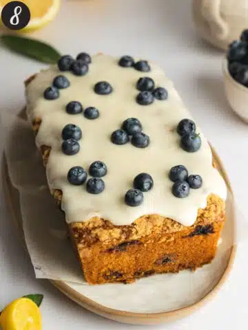 a loaf cake covered in icing with fresh blueberries on top.
