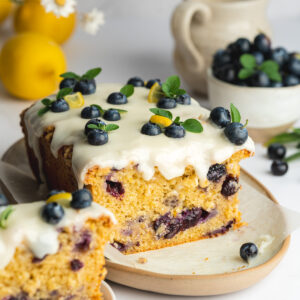 a freshly baked blueberry lemon loaf cake on an oval ceramic dish with icing and fresh blueberries on top.