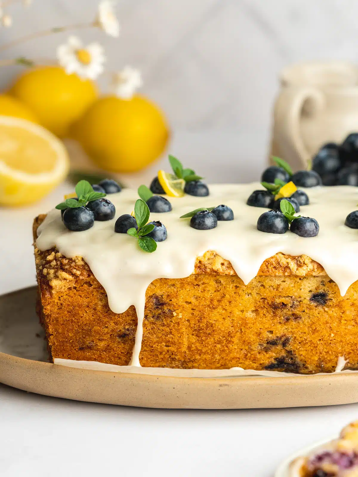 a loaf of blueberry lemon cake with icing pouring over the sides and fresh blueberries on top.