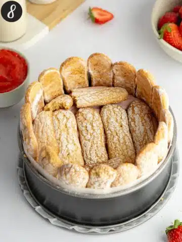 a second layer of ladyfinger cookies added on top of strawberry mousse in a cake pan.